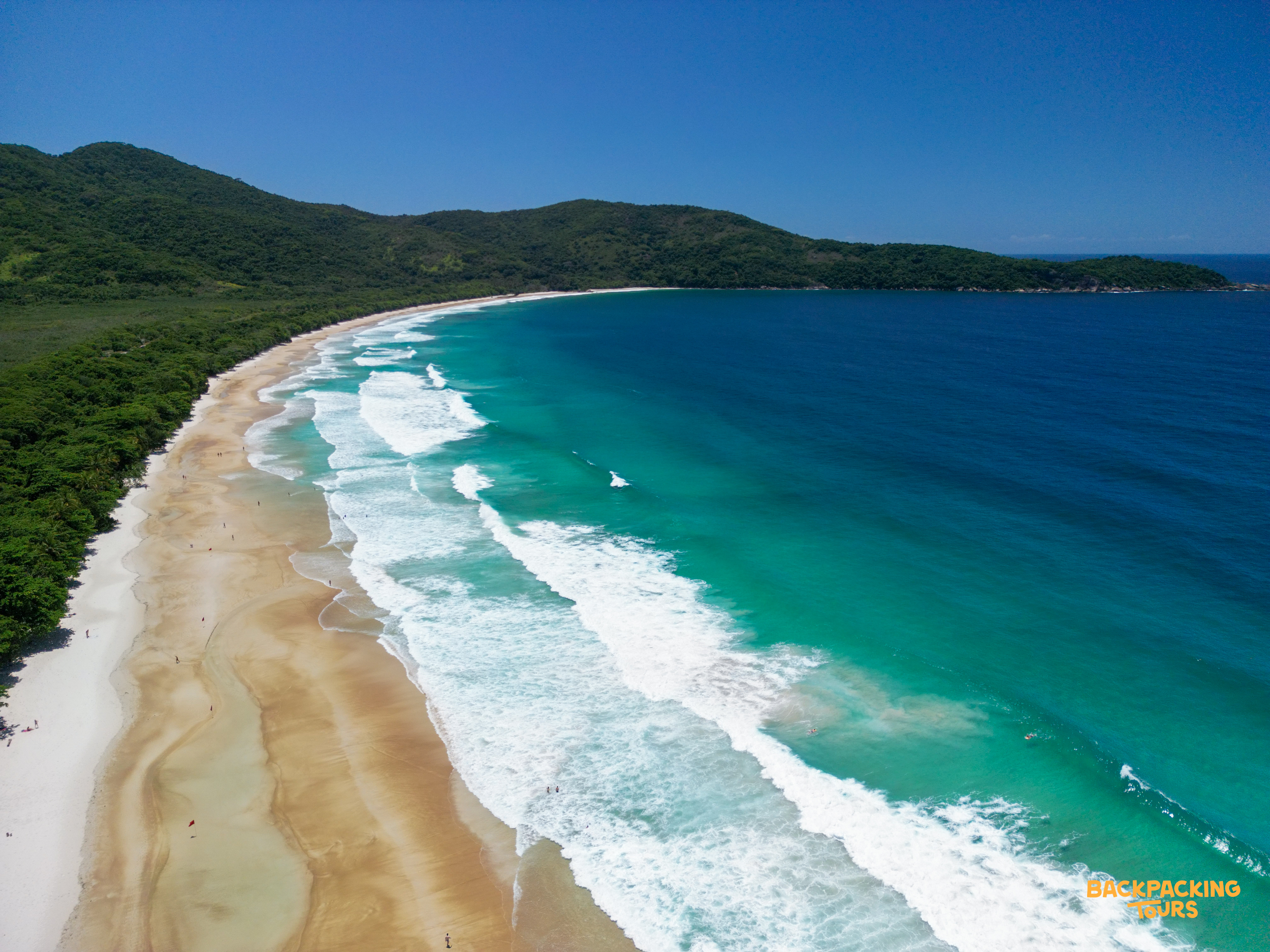 Lush green mountains meet white sand and clear turquoise waves at Lopes Mendes beach, Brazil.