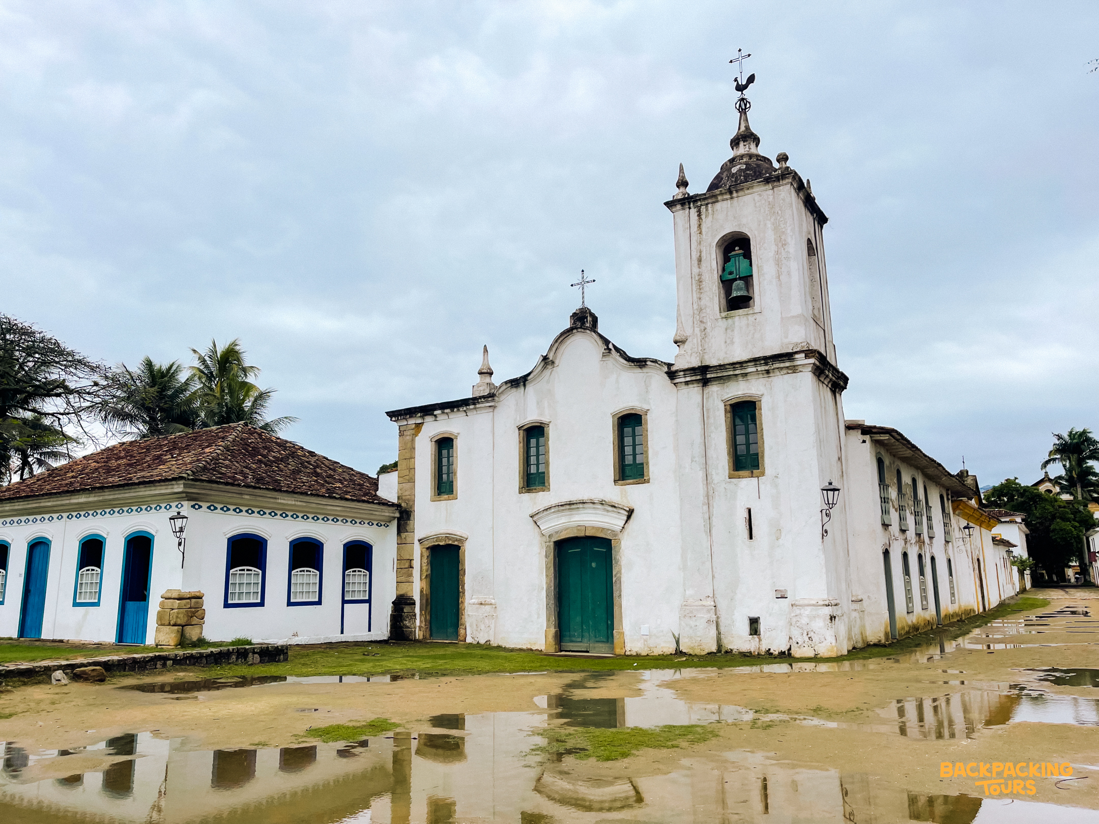 Historic white colonial church and building with green doors reflected in puddles in Paraty, Brazil.