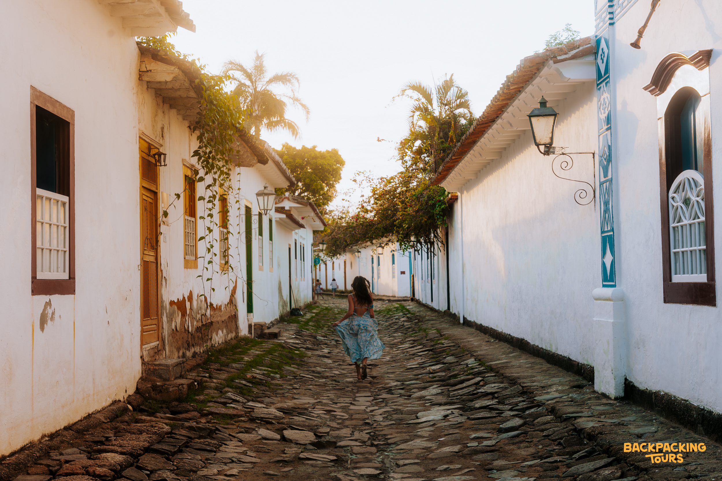 A woman strolls along a charming cobbled street lined with white colonial buildings in Paraty, Brazil.