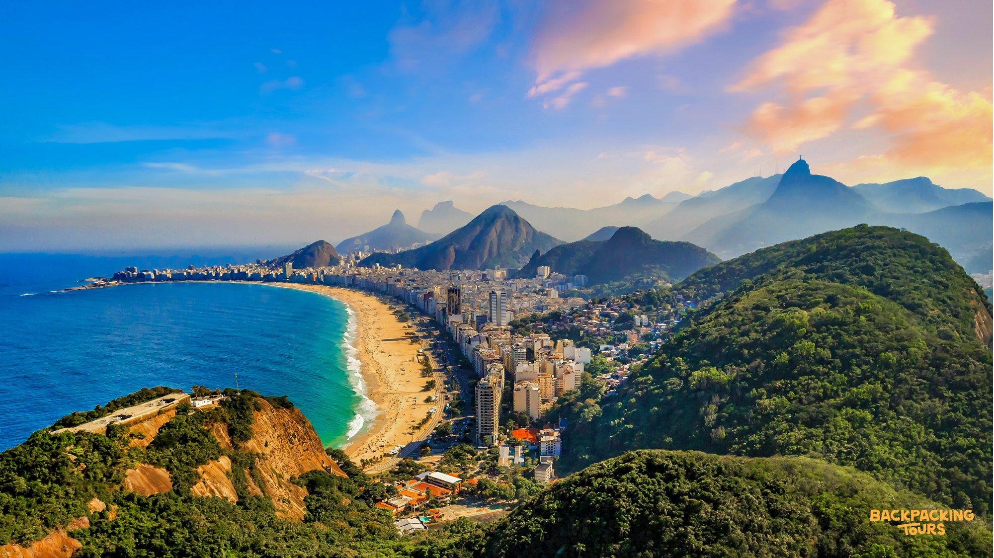 Panoramic view of Rio de Janeiro's iconic Copacabana beach, city, and mountains at sunset.