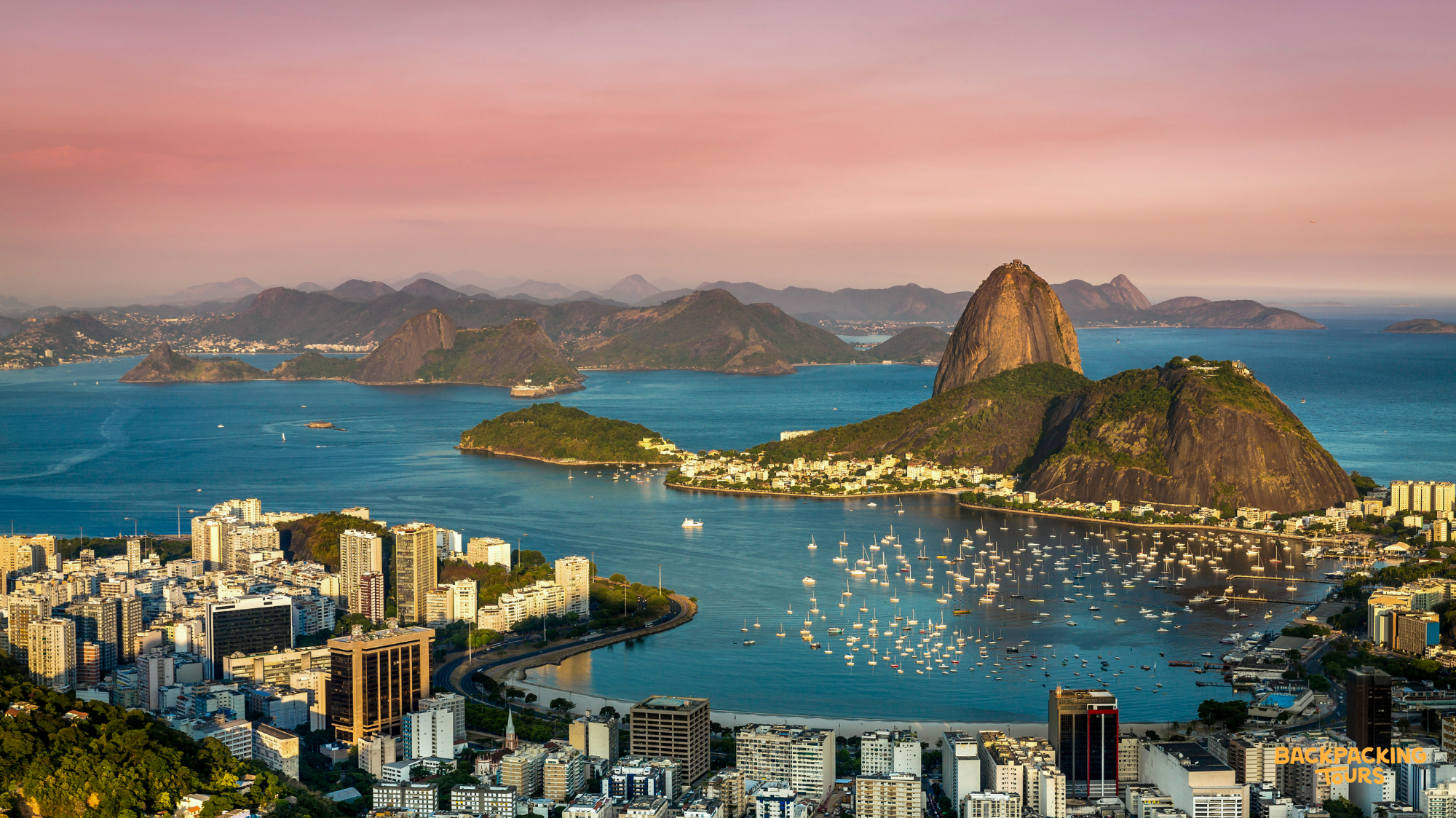 Aerial view of Rio de Janeiro's iconic Sugarloaf Mountain and bustling bay at sunset.