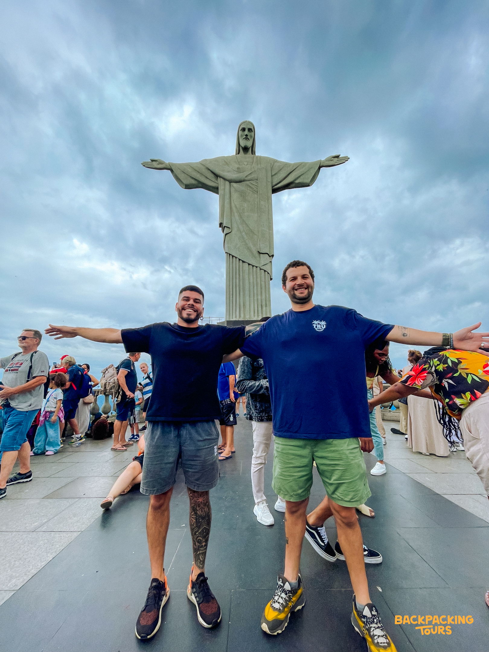 Two smiling men pose with outstretched arms in front of the iconic Christ the Redeemer statue in Rio.