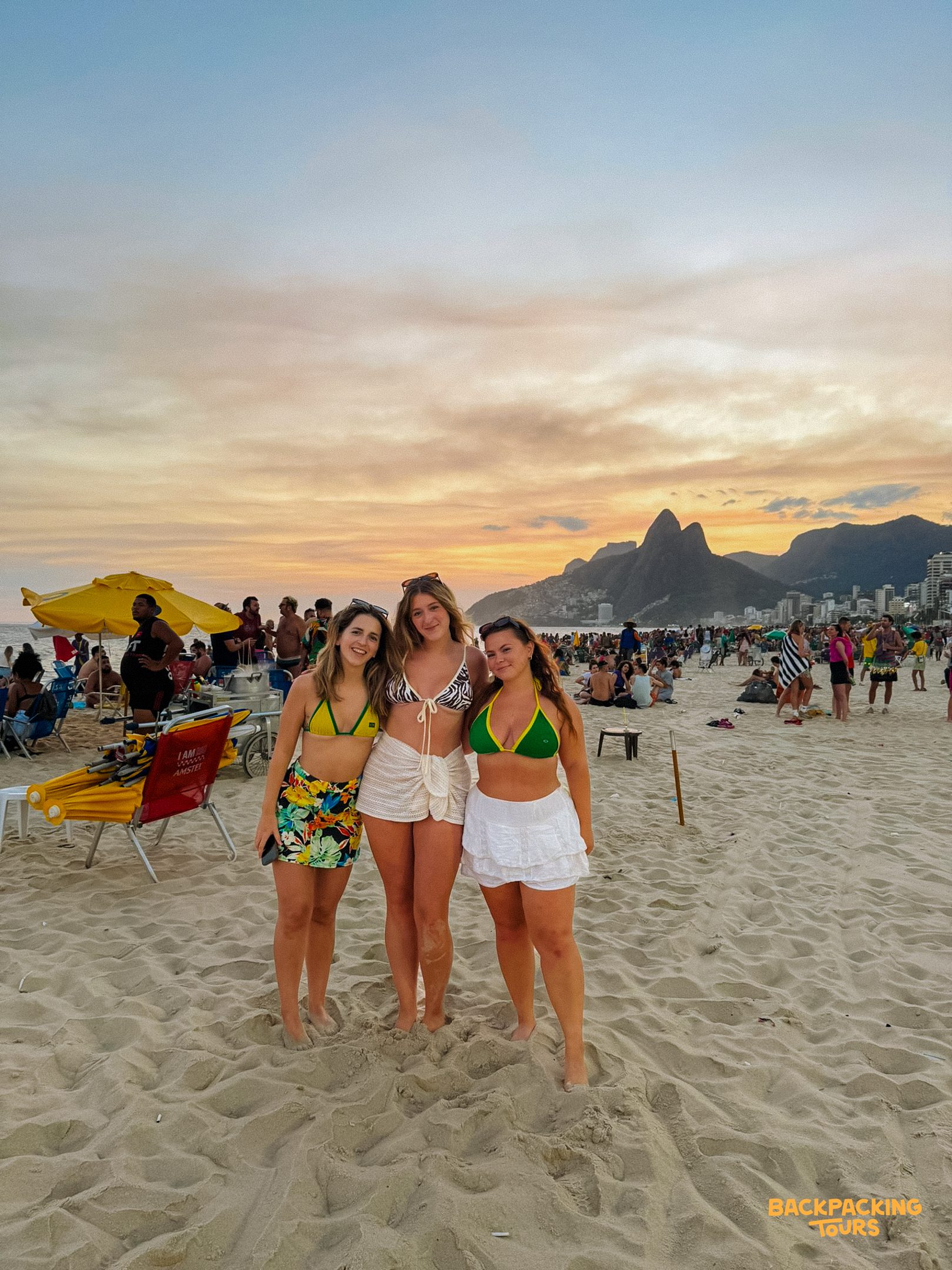 Three friends smiling on Copacabana Beach, enjoying a stunning sunset over the mountains of Rio de Janeiro.