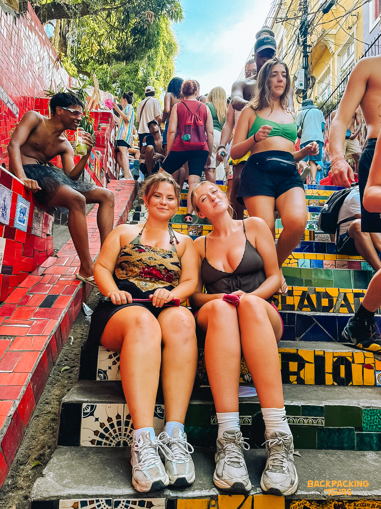 Friends relax and smile on the iconic, mosaic-covered Selarón Steps in sunny Rio de Janeiro.