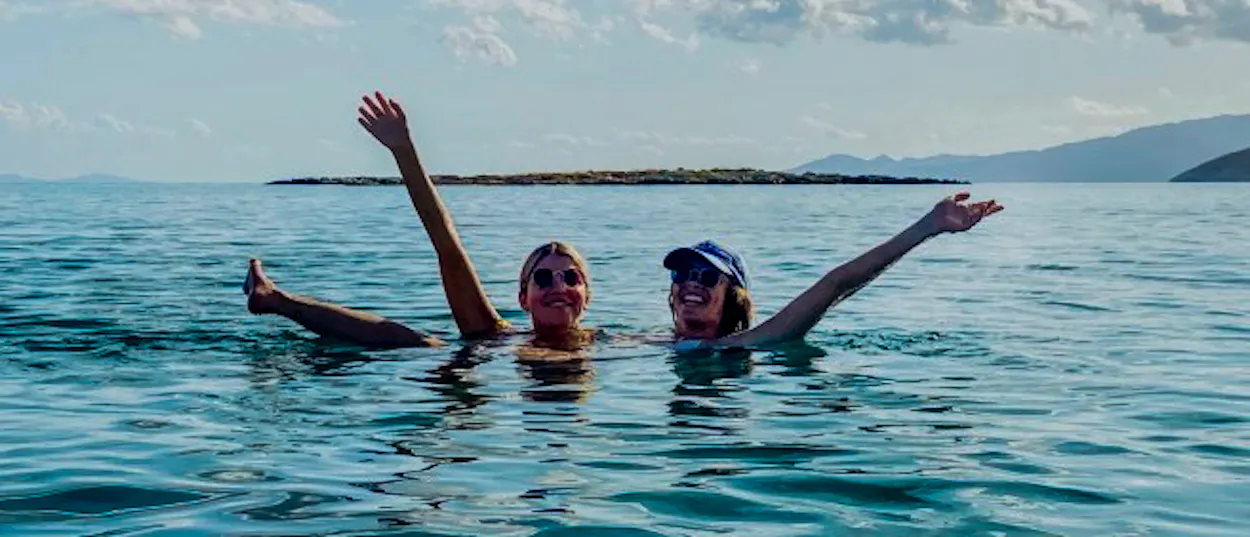 Two cheerful women splash and wave in the beautiful clear waters of Paraty bay.
