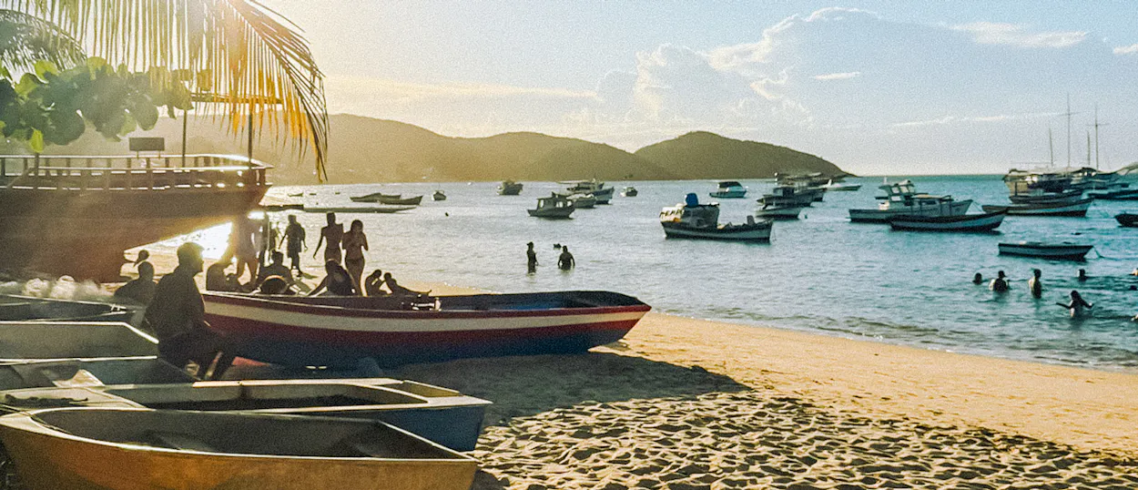 People swim and relax on a sandy beach with many boats in the calm waters of Ilha Grande, Brazil.