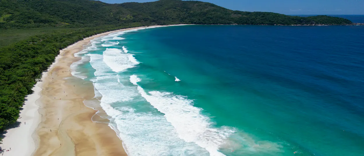 Beautiful Lopes Mendes beach in Brazil, featuring white sand, clear turquoise waves, and lush green forest.