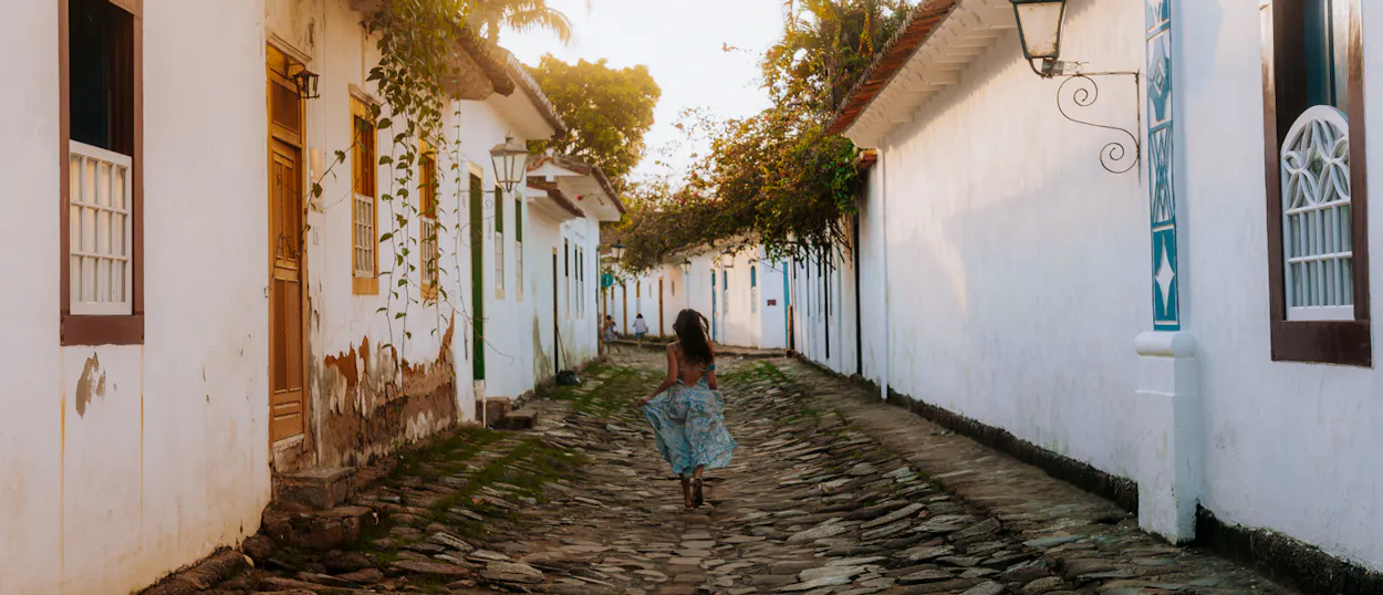A woman walks along a historic cobbled street lined with white colonial buildings in Paraty.