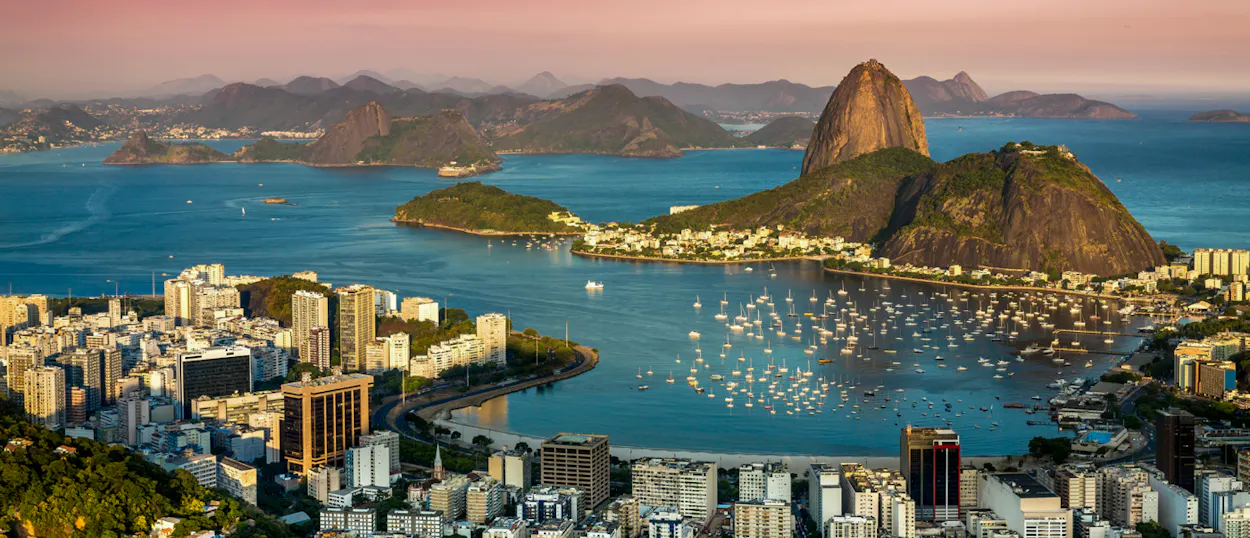 Panoramic view of Rio de Janeiro city, a bay filled with boats, and Sugarloaf Mountain.