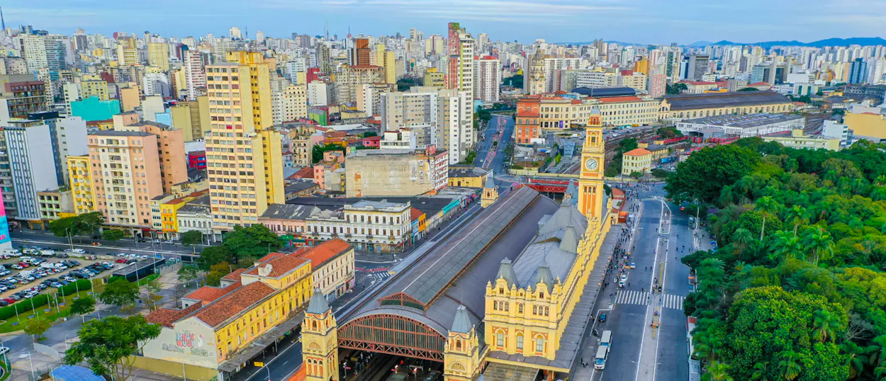 Historic train station with a clock tower, surrounded by a bustling city and green park in Sao Paulo.