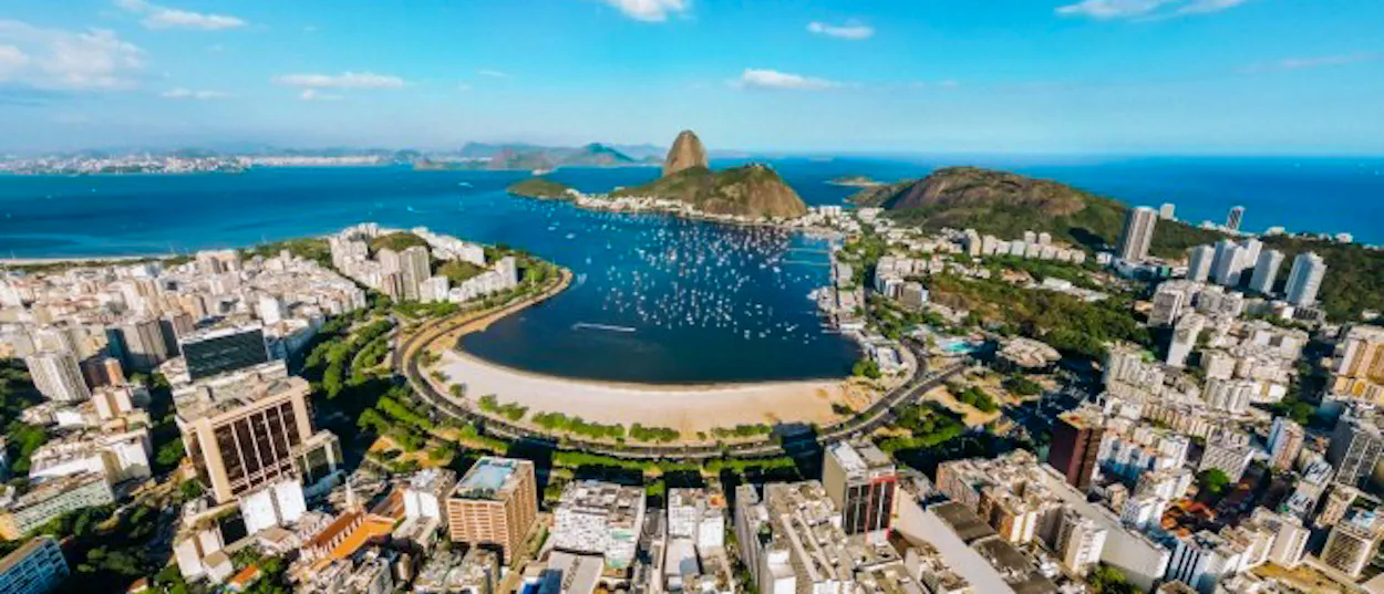 Panoramic view of Rio de Janeiro, featuring Sugarloaf Mountain, a bay with boats, and city buildings.