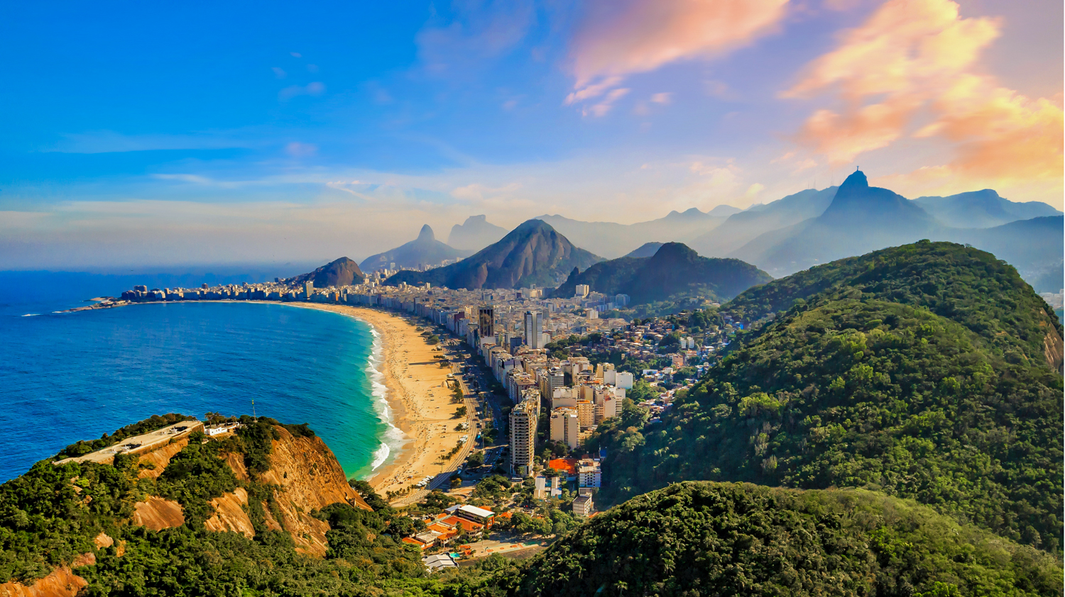 Rio de Janeiro's iconic Copacabana Beach and city skyline nestled between lush mountains at sunset.
