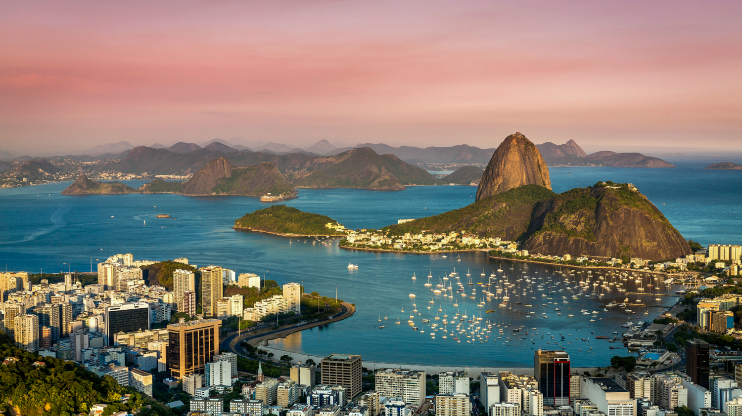 Panoramic view of Rio de Janeiro cityscape, Sugarloaf Mountain, and Guanabara Bay at sunset.