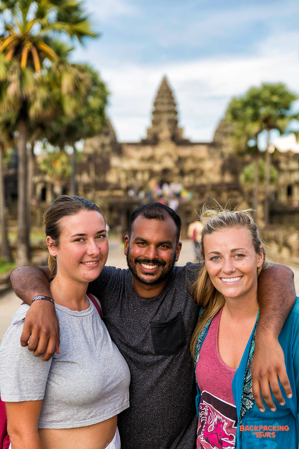 Three happy tourists pose with a local guide in front of the majestic Angkor Wat temple.