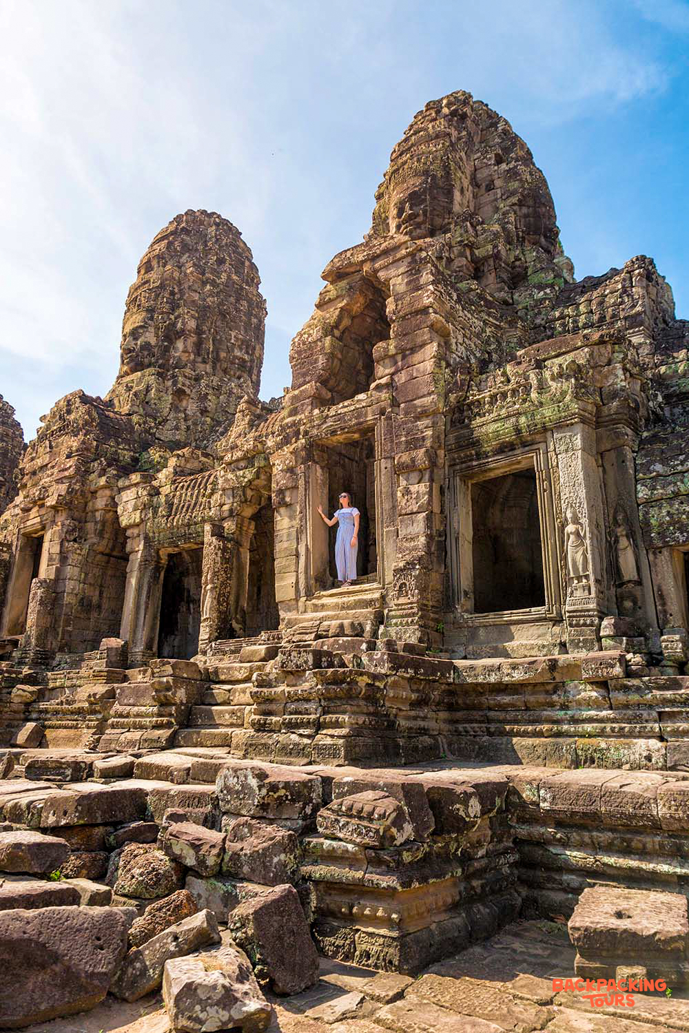 A woman explores the majestic ancient temple complex with towering stone faces in Siem Reap.