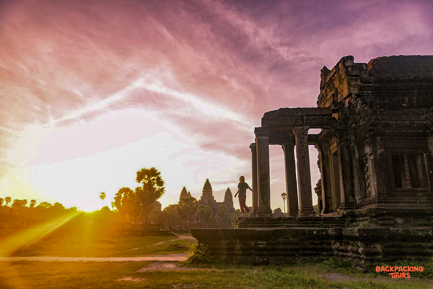 A lone figure stands on a stone temple at Angkor Wat, bathed in a vibrant sunrise.