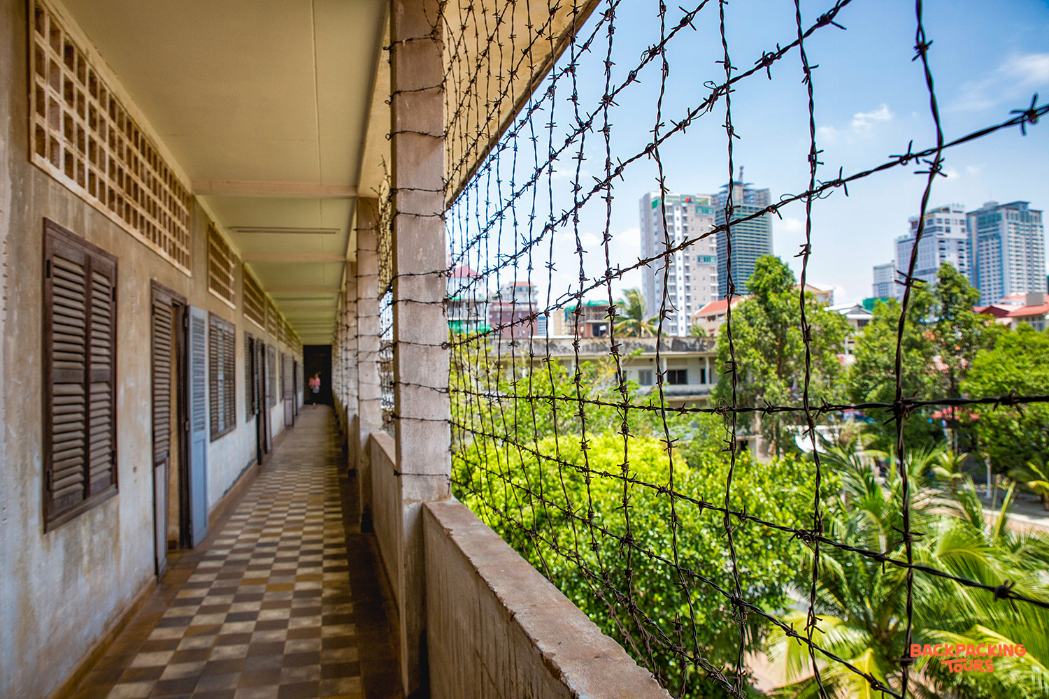 A somber hallway with barbed wire overlooks the modern cityscape of Phnom Penh, Cambodia.