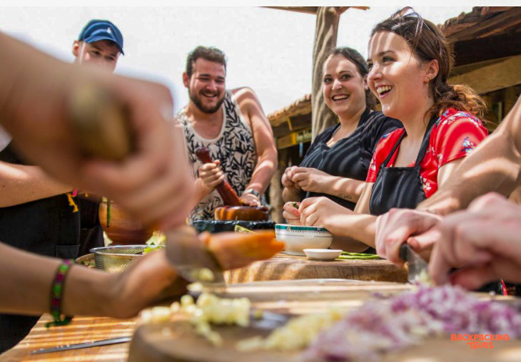 Travelers happily chop vegetables and grind spices during a Cambodian cooking class in Kampot.