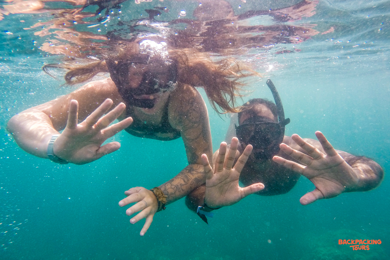 Two travelers snorkel in the clear turquoise waters of Koh Rong, playfully reaching out to the camera.