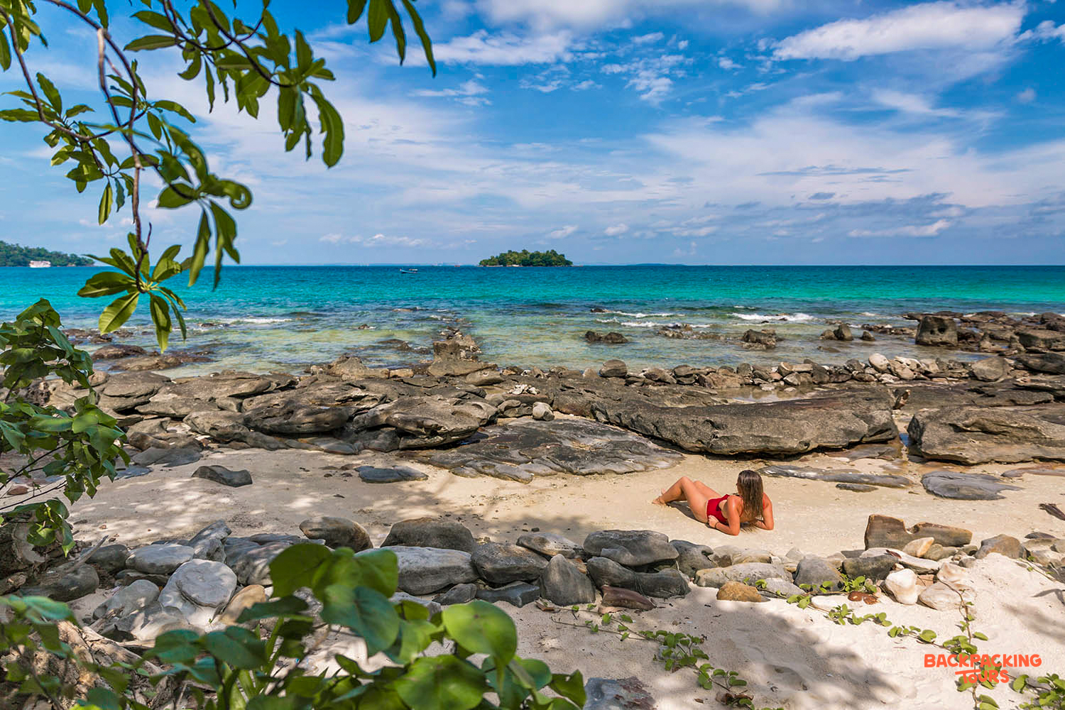 A person in a red swimsuit relaxes on a sunny beach in Koh Rong, enjoying the tropical ocean.