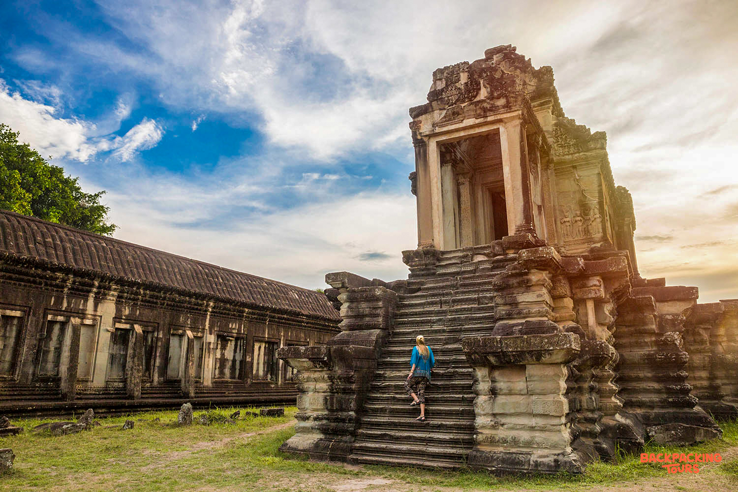 A backpacker ascends ancient stone steps of Angkor Wat temple under a vibrant blue sky in Cambodia.