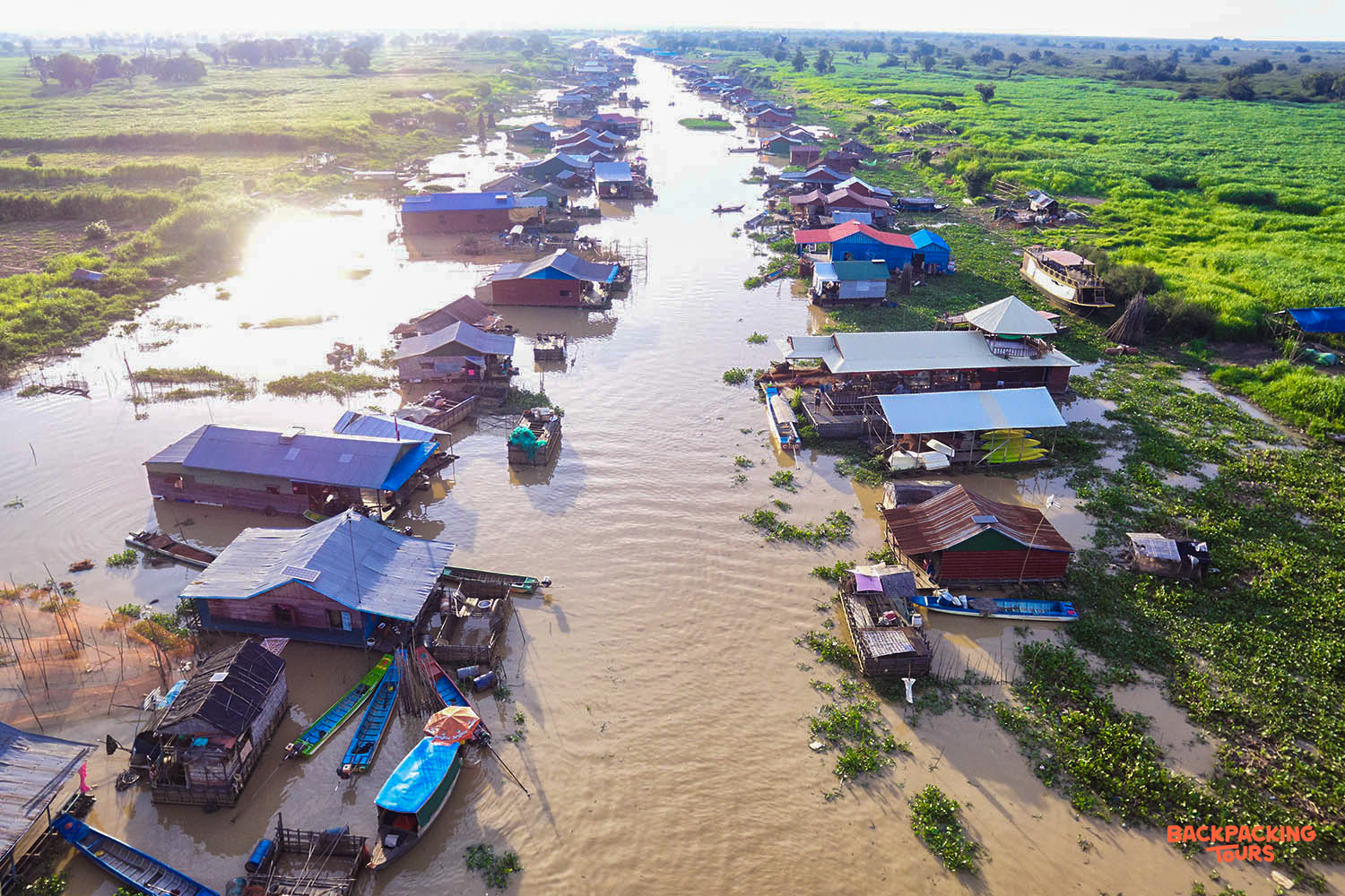 Aerial view of traditional floating houses and boats along a wide river in Siem Reap, Cambodia.
