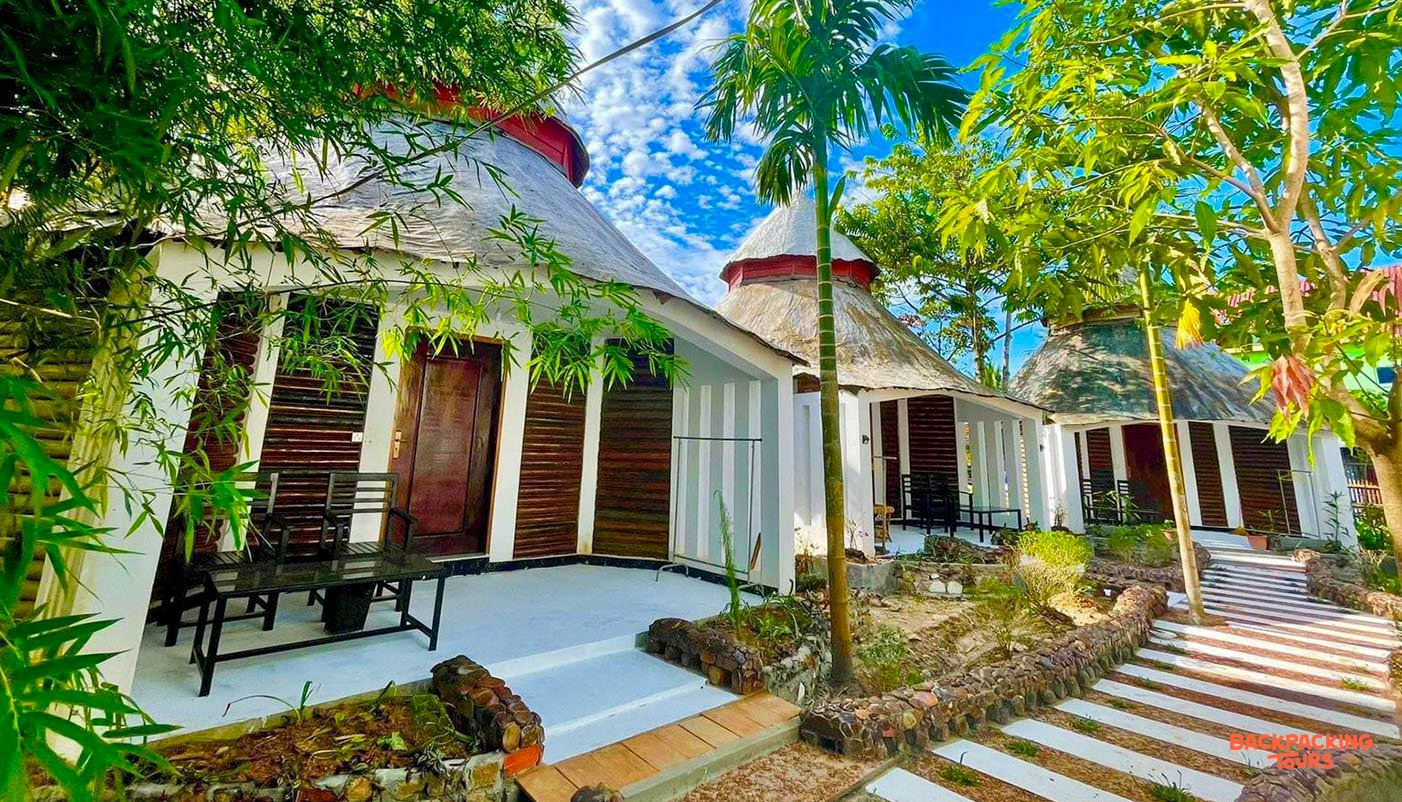 Charming thatched bungalows surrounded by lush tropical trees under a vibrant blue sky on Koh Rong Sanloem.