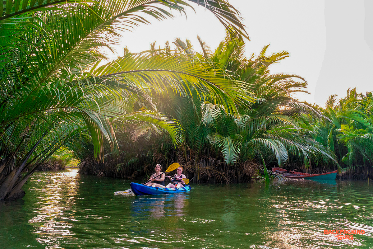 Two people kayak on a calm river surrounded by lush tropical palms in Kampot.