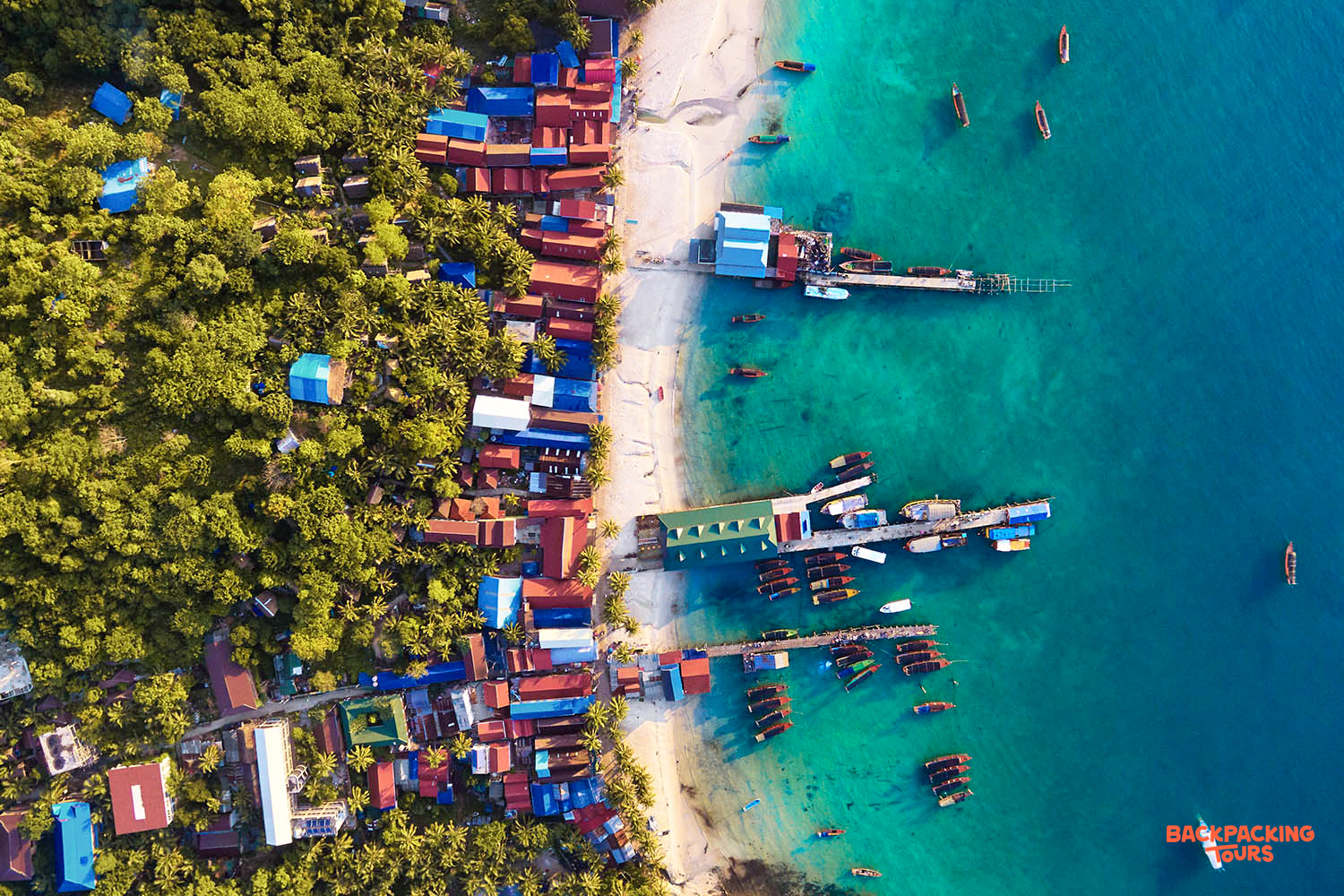 Vibrant aerial view of Koh Rong island, showing colorful village buildings, sandy beach, and many boats.
