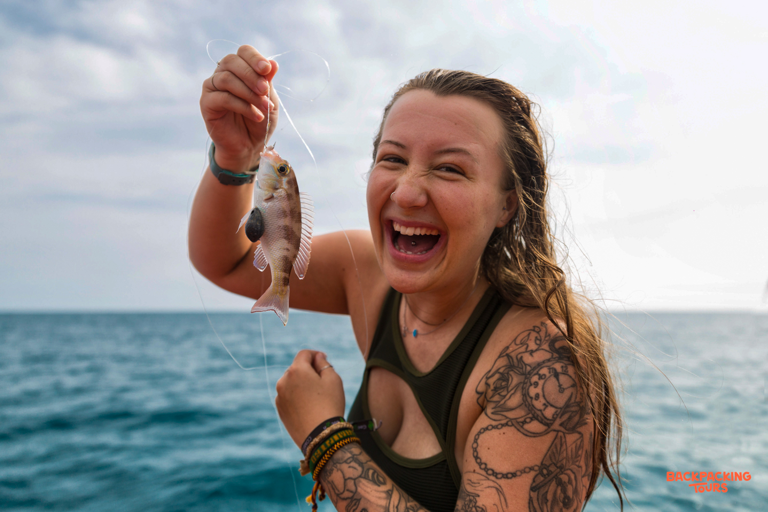 A happy woman on a boat trip at Koh Rong excitedly holds up her small catch.