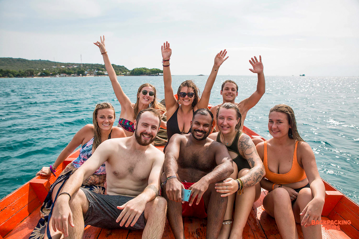 Joyful backpackers wave from a longtail boat, exploring the clear blue waters around Koh Rong.