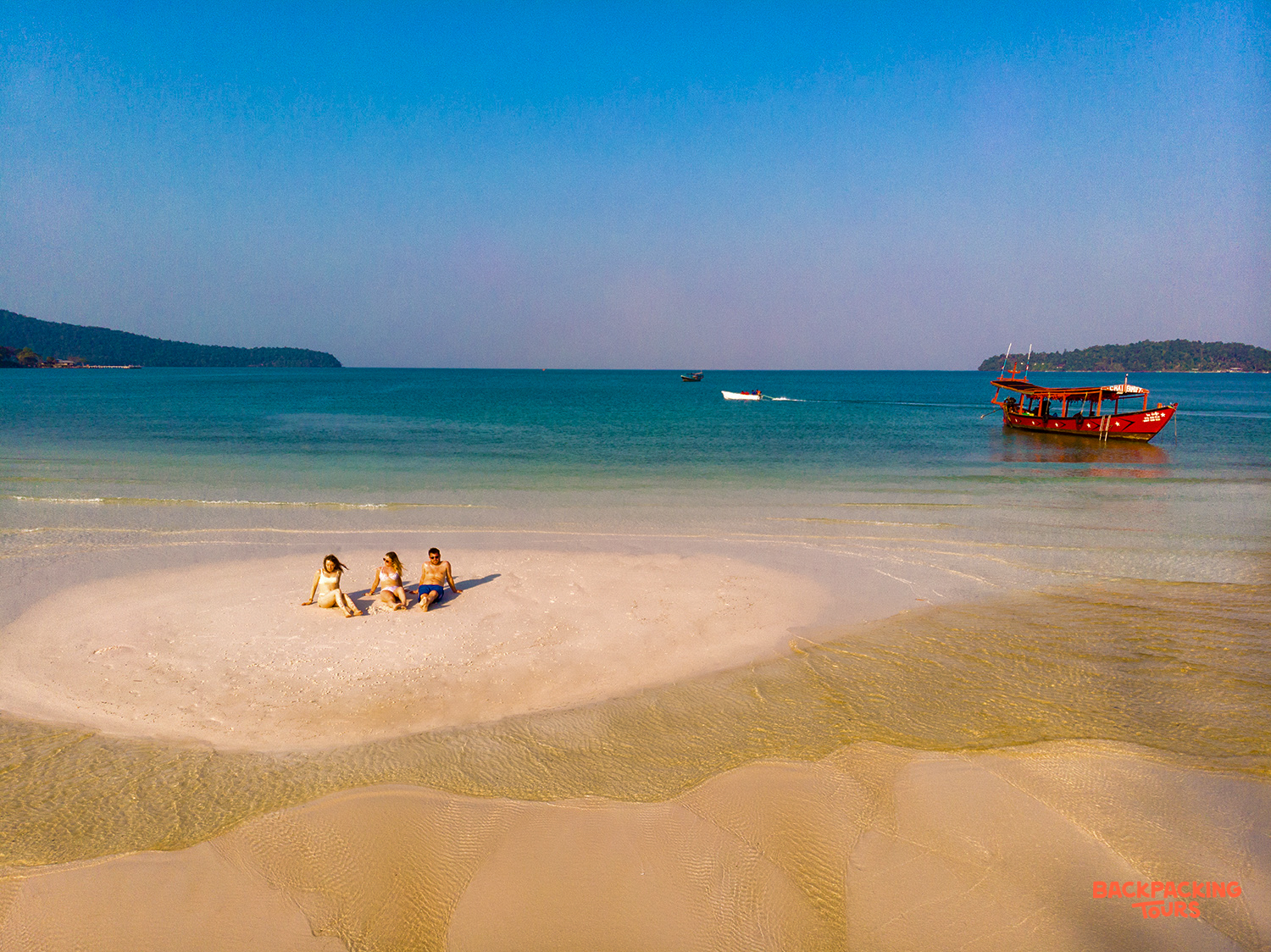 Three friends relax on a pristine sandbar in the clear turquoise waters of Koh Rong.
