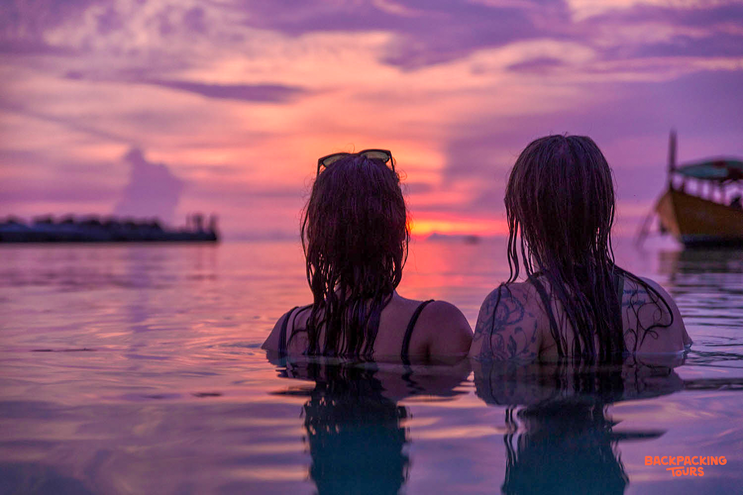 Relaxing in the water, two women admire the stunning purple and orange sunset over Koh Rong.