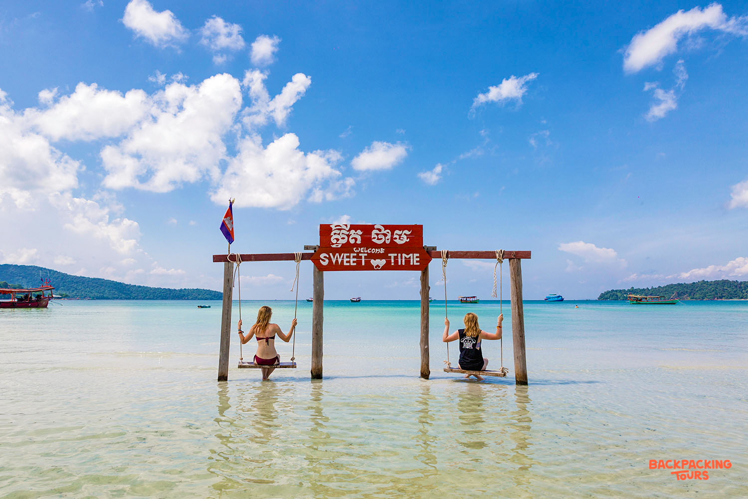 Friends relax on swings in the shallow, clear ocean water under a bright blue sky at Koh Rong.