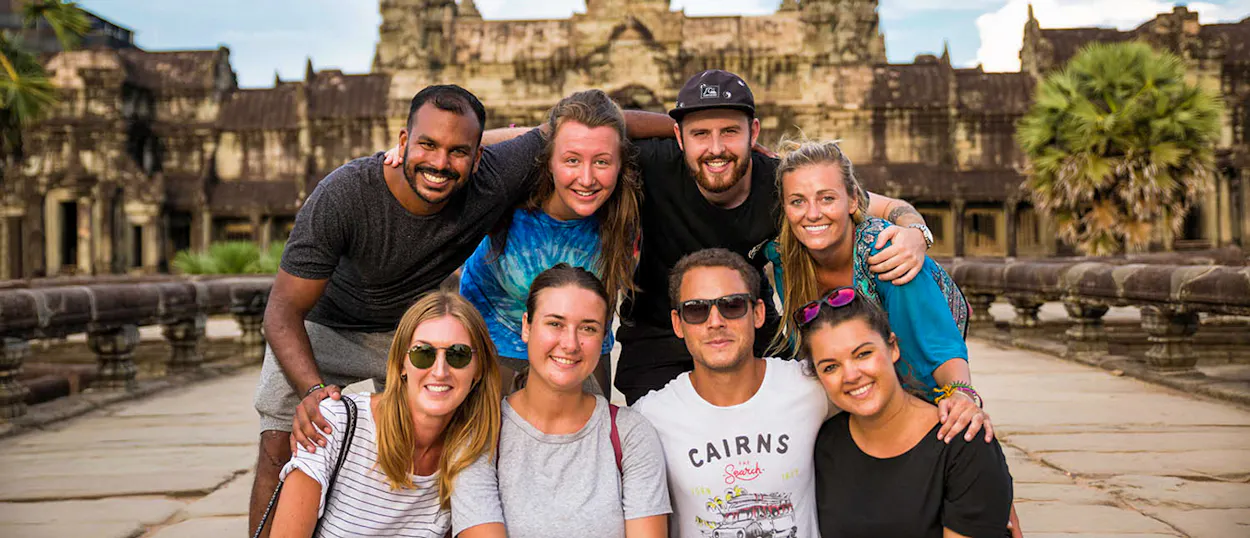 A happy group of eight friends smiling together in front of the majestic Angkor Wat temple in Cambodia.