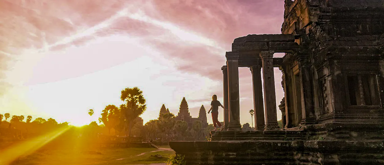 A traveler stands on ancient temple ruins at Angkor Wat during a stunning sunset.