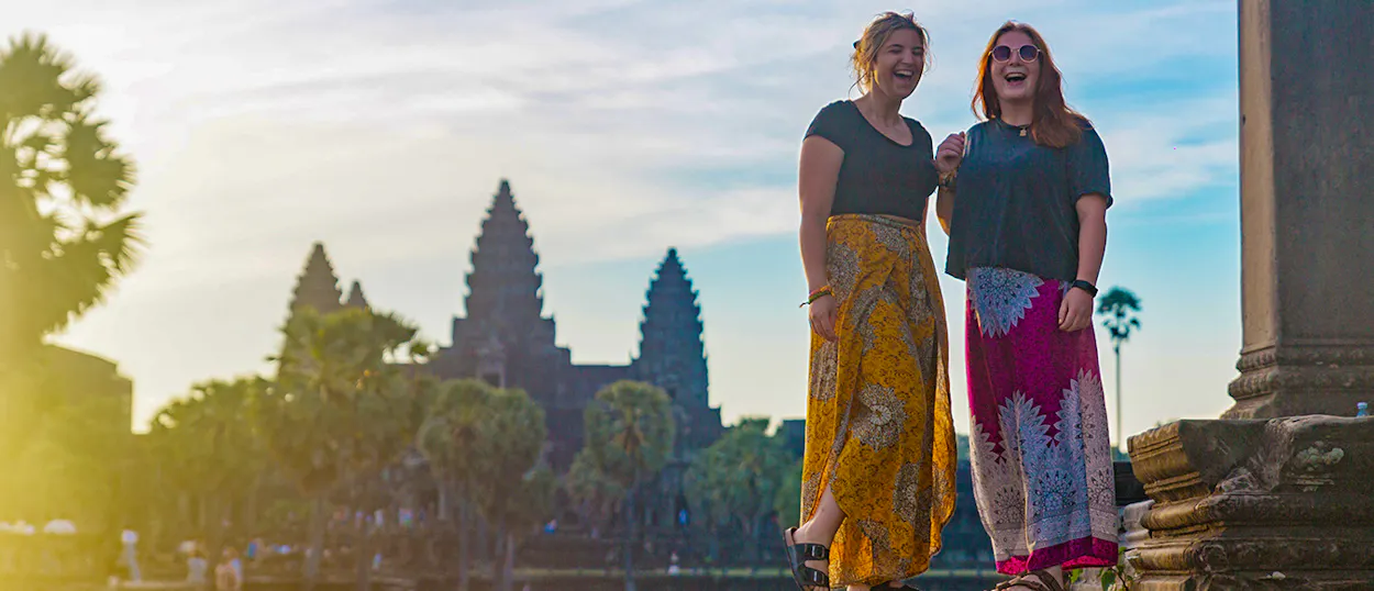 Two happy women laugh in front of the majestic Angkor Wat temple at sunrise.