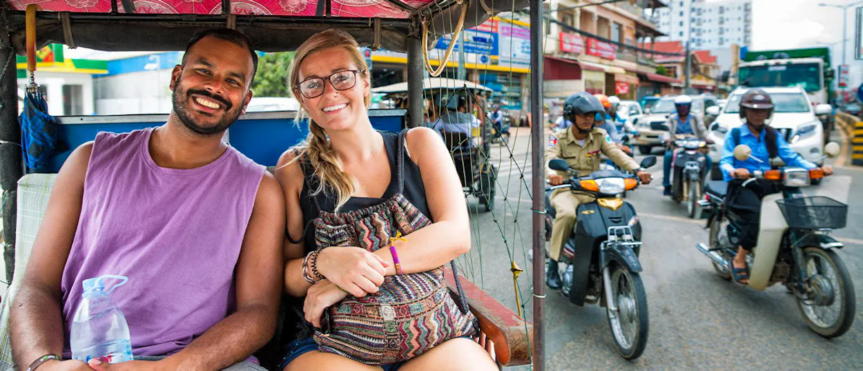 Two smiling travelers riding in a tuk-tuk on a busy street in Phnom Penh.