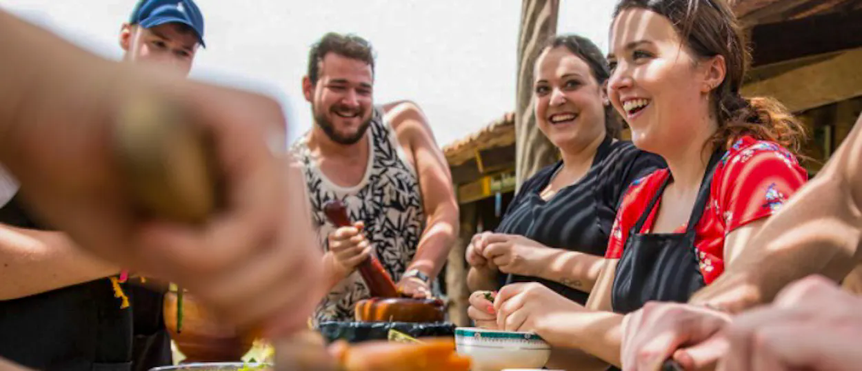 Happy travelers enthusiastically preparing local dishes during an outdoor cooking class in Kampot.