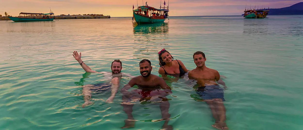 Four happy friends swim in the clear turquoise ocean during a beautiful sunset in Koh Rong.