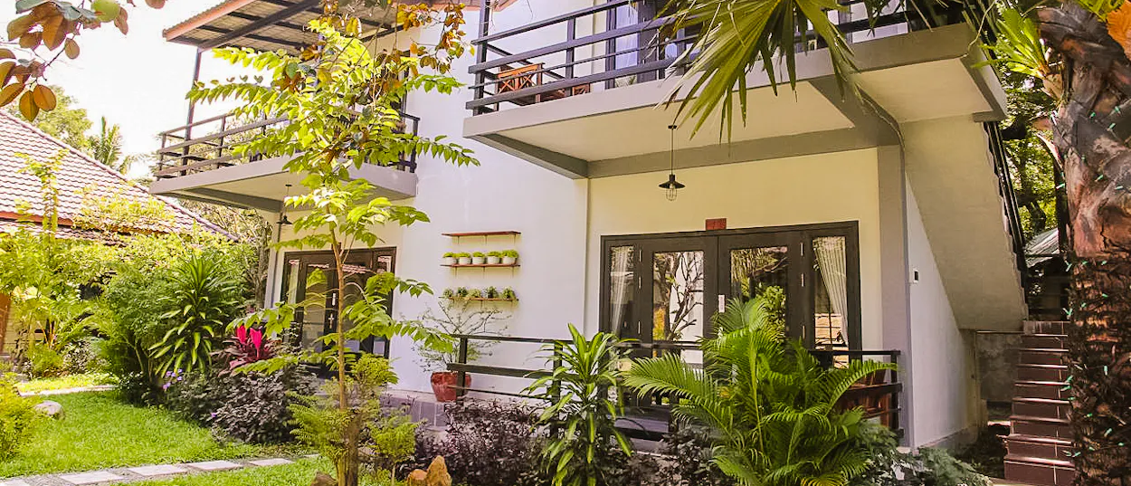 A charming two-story guesthouse with balconies nestled among lush tropical plants in Kampot.