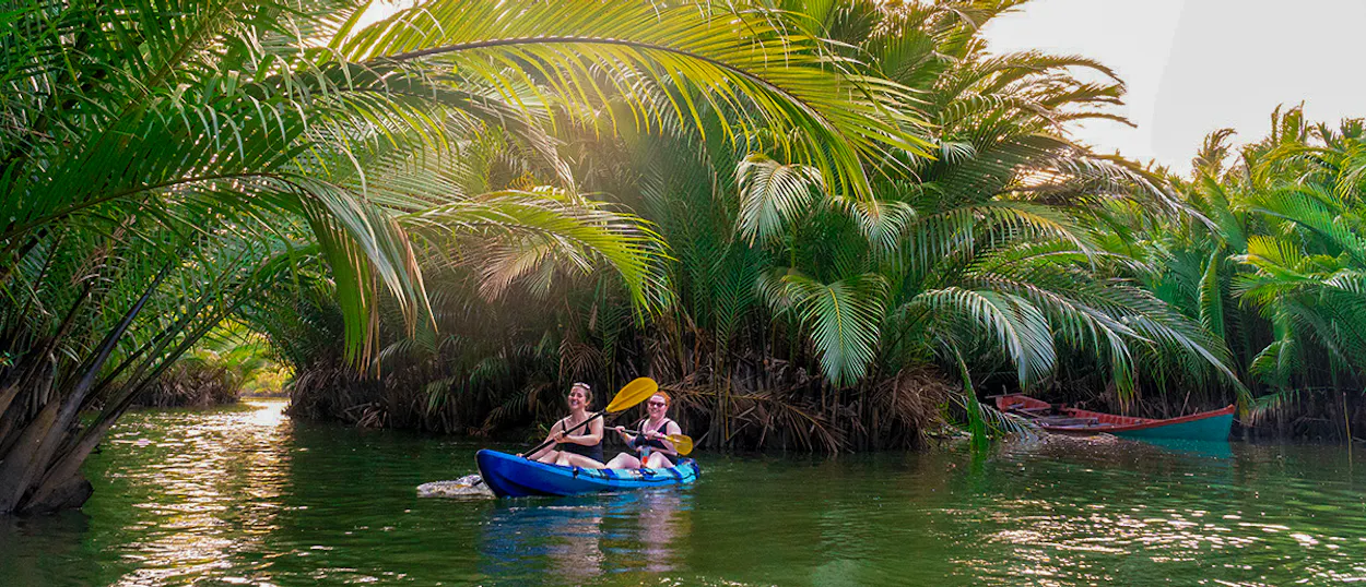 Two people enjoy kayaking on a serene river surrounded by lush palm trees in Kampot.