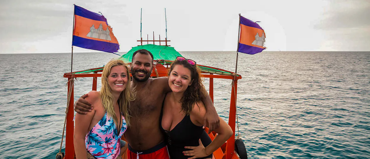 Smiling friends on a longtail boat with Cambodian flags, enjoying a trip on Koh Rong.
