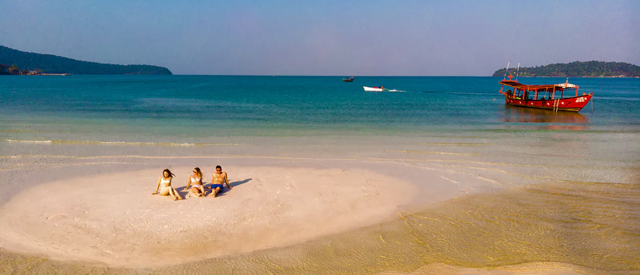Three friends relax on a sandbar in the clear turquoise waters of Koh Rong, Cambodia.