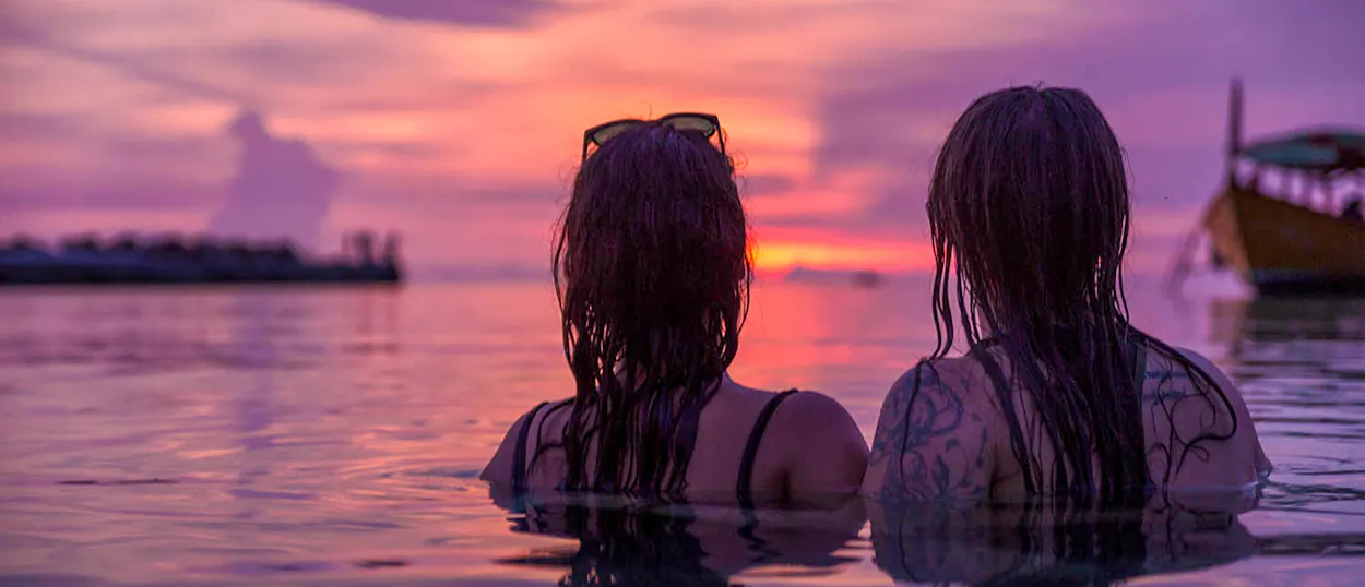 Two women relax in the calm ocean, watching a beautiful pink and orange sunset over Koh Rong.