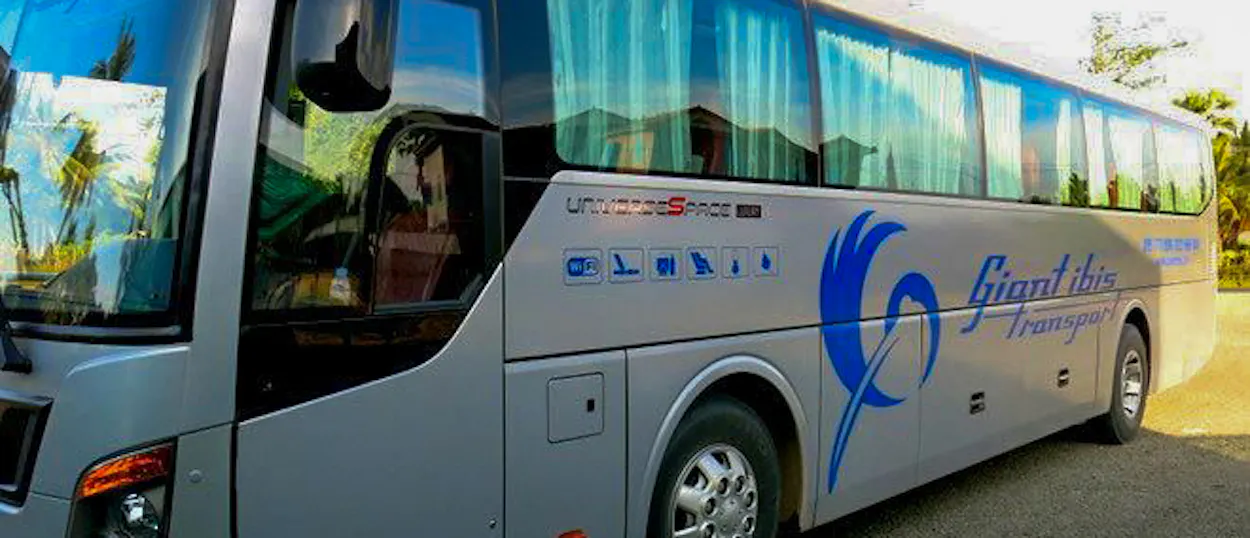 A modern silver Giant Ibis overnight bus with blue branding and curtains, parked in Cambodia.