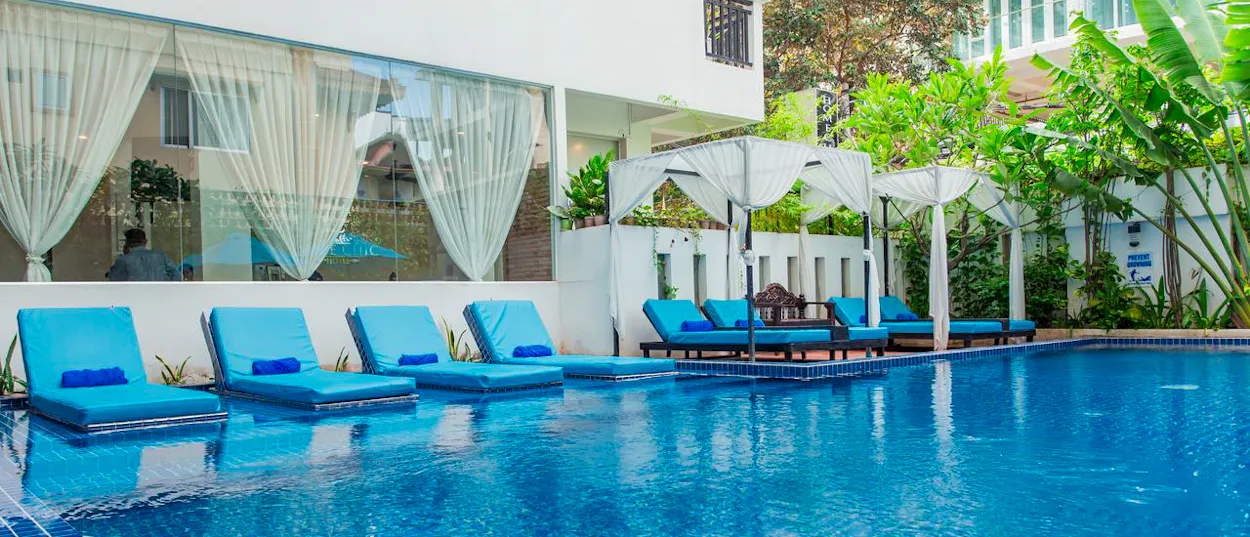 Inviting blue swimming pool with submerged lounge chairs and shaded cabanas at a Phnom Penh hotel.