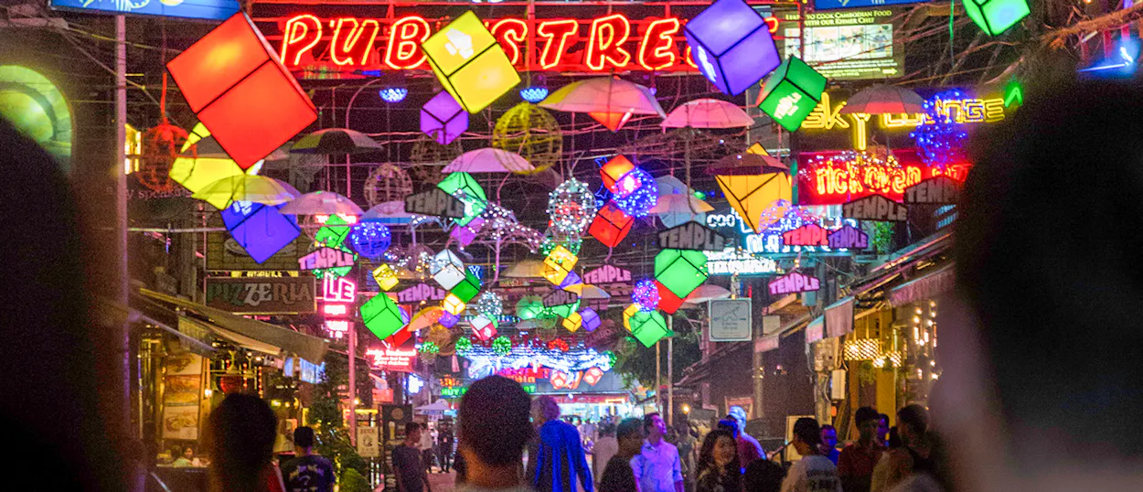 People walk along Pub Street in Siem Reap, illuminated by colorful lanterns and neon signs at night.