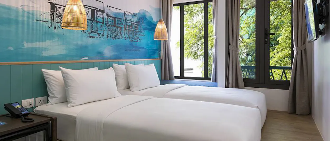 A bright, modern hostel room in Siem Reap with two beds and a mural of floating houses.