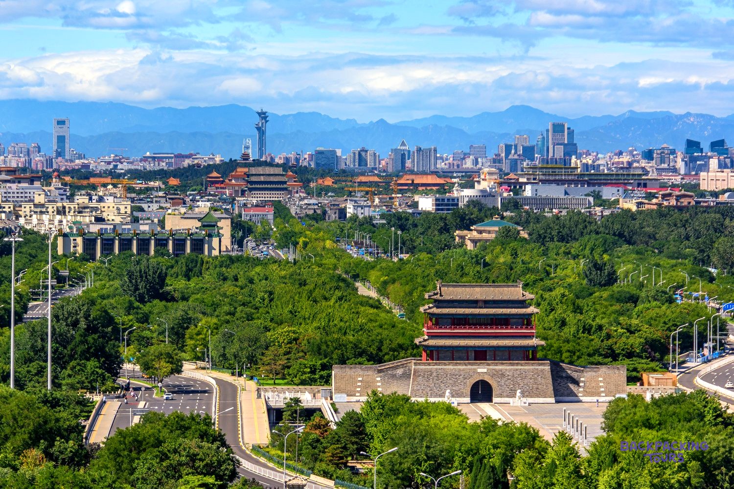 A traditional city gate tower stands in green parkland, with Beijing's skyline and mountains beyond.